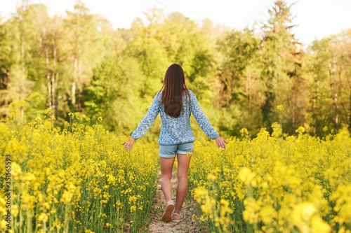 Spring portrait of happy young woman posing in colza field, back view