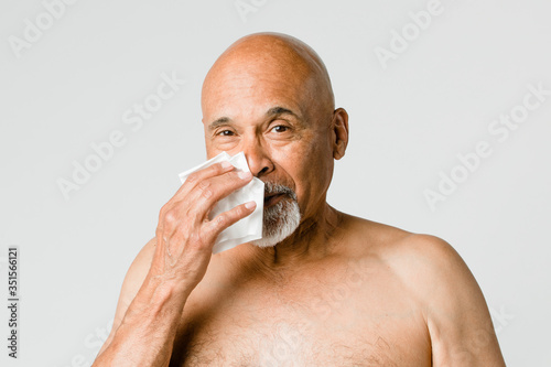 Coronavirus infected senior man blowing nose into a tissue paper