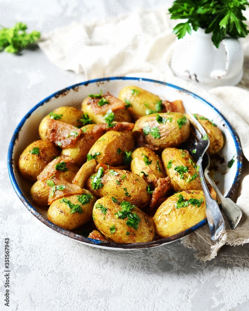 Young baked potato with bacon, spices and herbs in a baking dish on a gray background, still life Young baked potato with bacon, spices and herbs in a baking dish on a gray background, still life