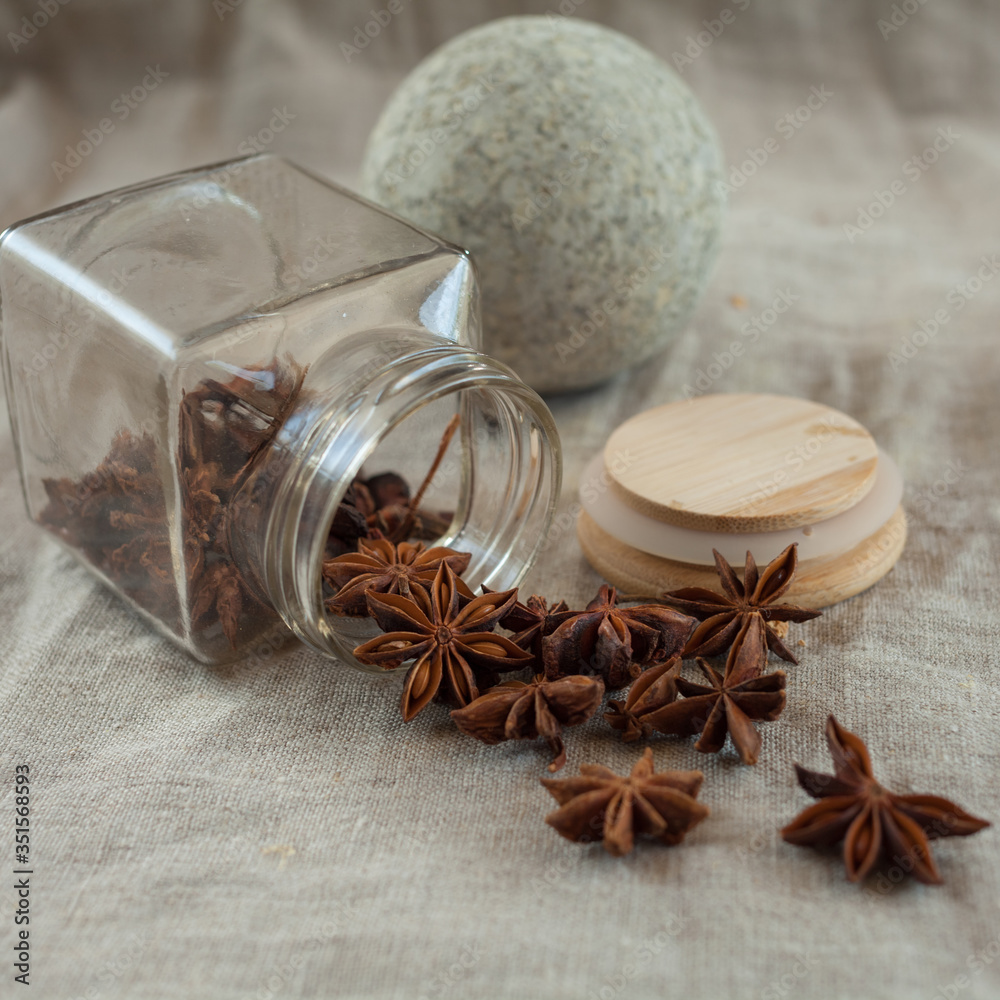 A stone ball for grinding spices and a glass jar with scattered spices on a linen tablecloth. Anise star A stone ball for grinding spices and a glass jar with scattered spices on a linen tablecloth. Anise star