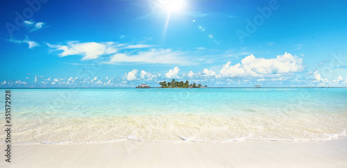 Beautiful sandy beach with white sand and rolling calm wave of turquoise ocean on Sunny day. White clouds in blue sky. Maldives, perfect scenery landscape, copy space, panoramic view.