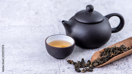 Hot tea in black teapot and cups and dry tea leaves over bright gray cement background, close up, copy space design concept.