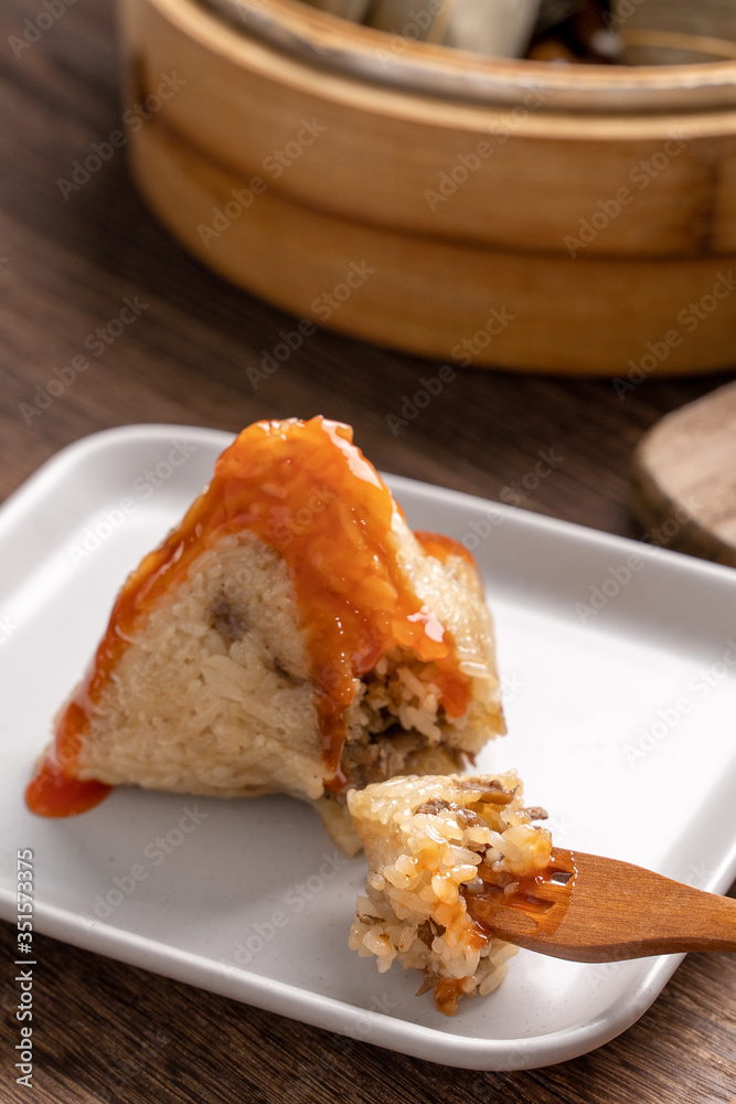 Dragon Boat Festival food - Rice dumpling zongzi, young Asian woman eating Chinese traditional food on wooden table at home celebration, close up Dragon Boat Festival food - Rice dumpling zongzi, young Asian woman eating Chinese traditional food on wooden table at home celebration, close up