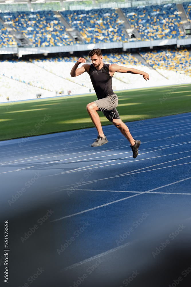 selective focus of fast handsome runner exercising on running track at stadium