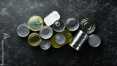 Set of tin cans with food on black stone background. Food stocks. Top view. Free space for your text.