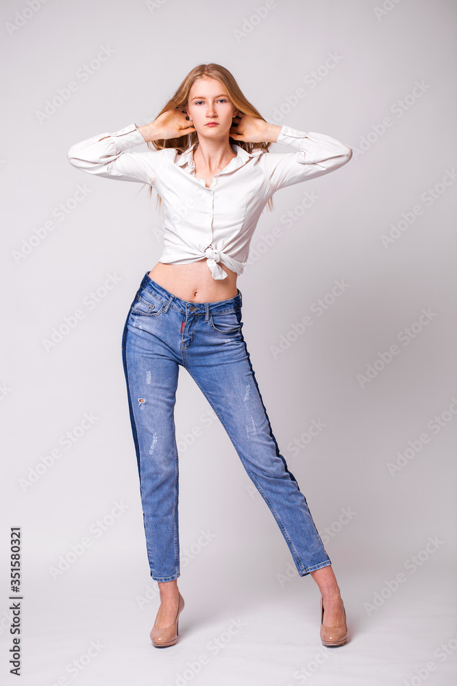Young beautiful blonde girl in a white shirt. Studio gray isolated background