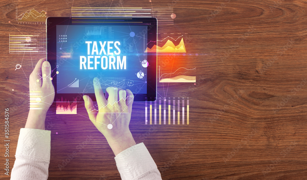 Close-up of hands holding tablet with TAXES REFORM inscription, modern business concept
