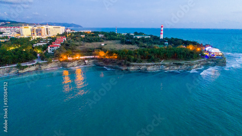 Evening panorama of Gelendzhik resort from a bird's-eye view. "Thick" Cape, Gelendzhik lighthouse. The lights of the embankment are reflected in the dark blue water