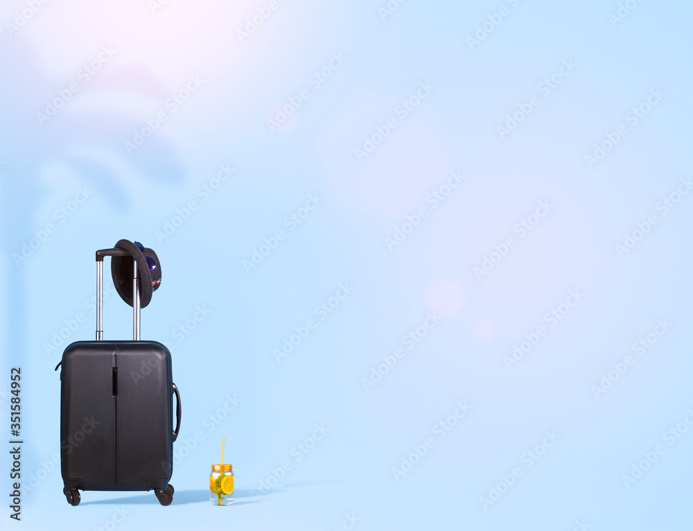 Black suitcase with hat, sun glasses and a fresh cocktail on a soft blue background. Minimal travel concept with copyspace