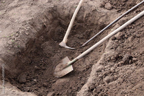 Digging a pit. Pit in the ground. The shovel, pickaxe and crowbar lay in the pit. photo