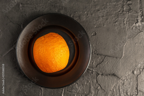 a whole orange orange on a smooth black plate and a textured black background