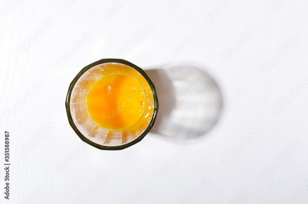 Top view of glass cup and fresh broken egg yolks in it on the white kitchen table.Empty space Top view of glass cup and fresh broken egg yolks in it on the white kitchen table.Empty space
