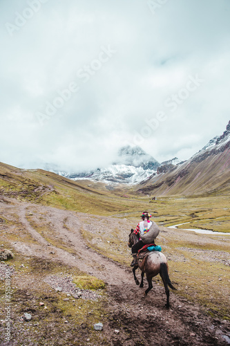 Traditional indigenous Quechua horseman rides his horse across the valleys of the Cusco region of Peru, next to Rainbow Mountain (or Montaña de Siete Colores) © Lozzy