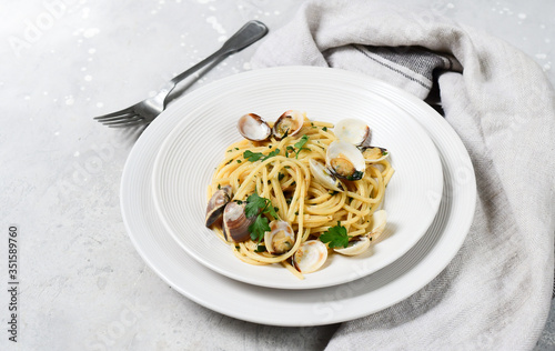Traditional italian food seafood pasta with clams and parsley Spaghetti alle Vongole in white plates on a grey background. top view