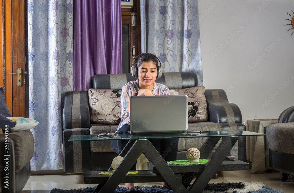 Obraz premium Young Indian girl is doing online study from home during lockdown by using laptop and headphone