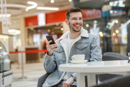 guy sitting at a table in an empty shopping center and looking at the phone