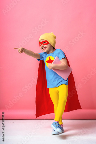 cheerful child dressed in superhero costume and a hat with a book in his hands.