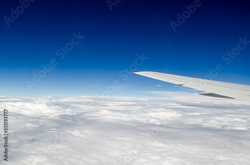 The wing of a flying plane against the background of thick white clouds. View from the porthole to the wing of the plane and the sky. Flying above the clouds. Opening season for travel and relaxation. © Ninaveter