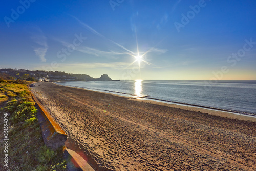 Image of Grouville bay with Gorey Castle in the background with a smooth sea at sunrise with the beach and blue sky. Jersey, Channel Islands, UK photo