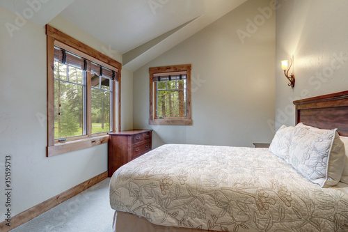 Beautiful calm soft grey bedroom interior with vaulted ceiling, lots of indows and light color bedding.