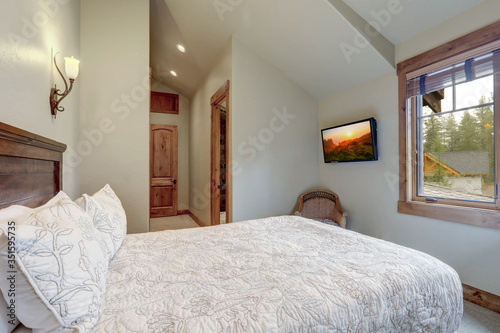 Beautiful calm soft grey bedroom interior with vaulted ceiling, lots of indows and light color bedding.