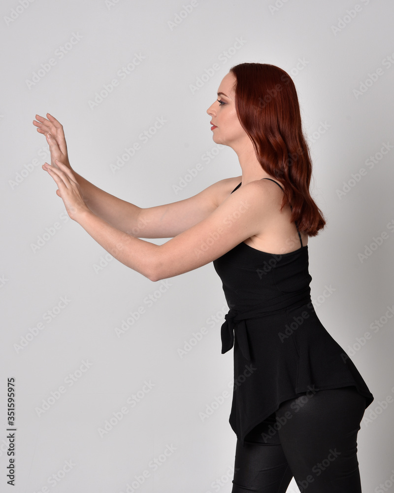 3/4 portrait of a pretty girl with red hair wearing black leather pants and top. isolated against a studio background 3/4 portrait of a pretty girl with red hair wearing black leather pants and top. isolated against a studio background