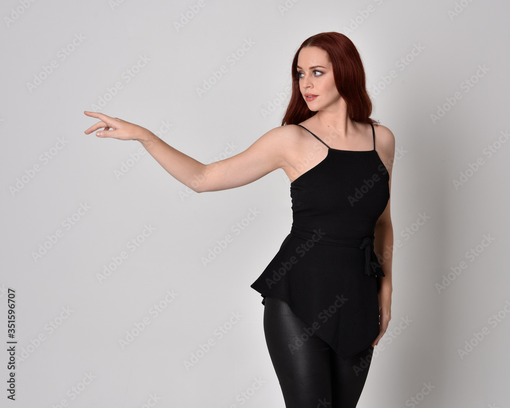 3/4 portrait of a pretty girl with red hair wearing black leather pants and top. isolated against a studio background 3/4 portrait of a pretty girl with red hair wearing black leather pants and top. isolated against a studio background