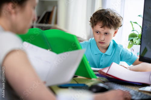 schoolboy sits at table with his mother and does homework, looking at textbook