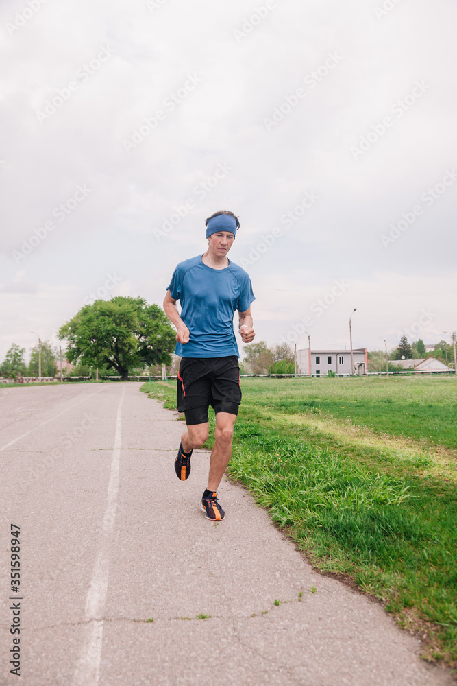 Fototapeta premium A young athlete in a blue T-shirt runs around the stadium