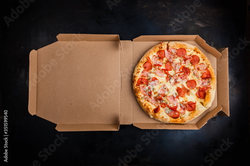 Pizza in a cardboard box against a dark background. Space for text. View from above. Pizza delivery. Pizza menu.