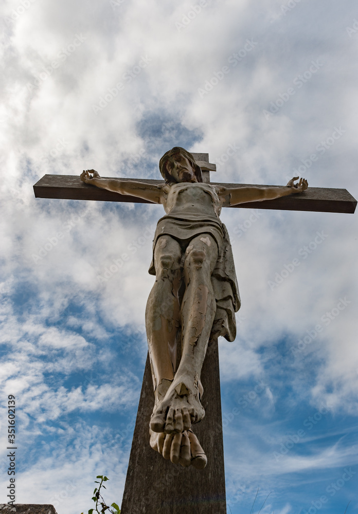 Looking up at old weathered Jesus crucifixion statue in a rural Irish cemetary, cloudy blue skies background