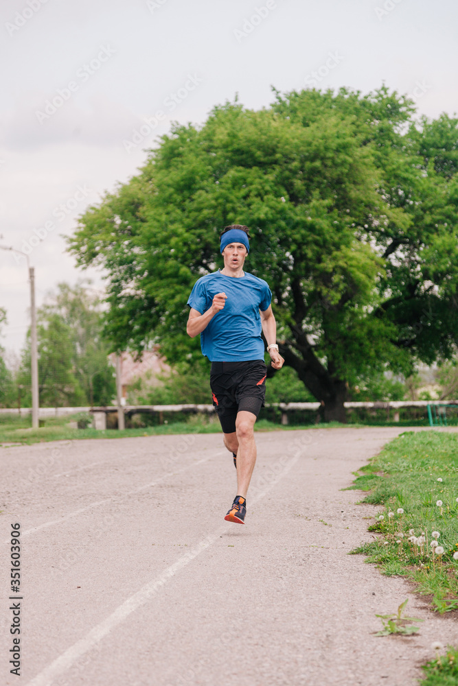 Fototapeta premium A young athlete in a blue T-shirt runs around the stadium