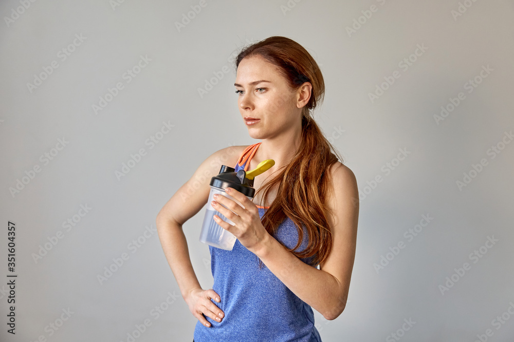 A sports girl in a gray background with water in her hand. A sports girl in a gray background with water in her hand.
