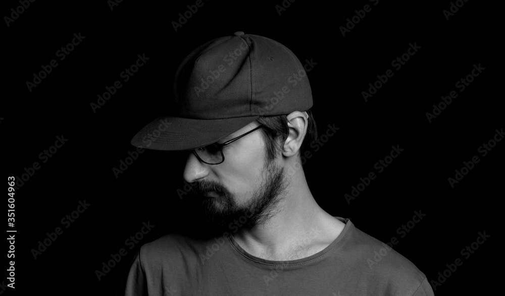 portrait of a guy with a beard in glasses and a cap on a black background