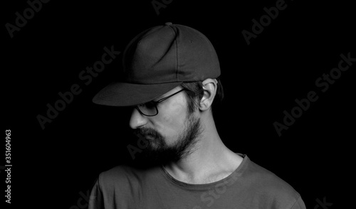 portrait of a guy with a beard in glasses and a cap on a black background © Serhii  Holdin