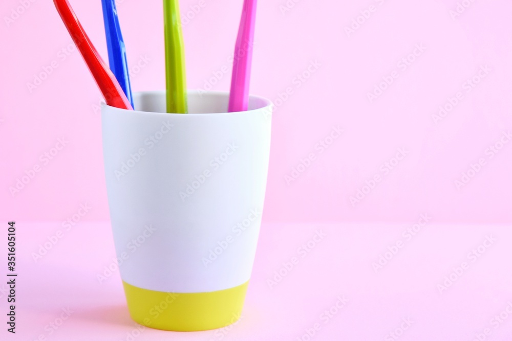 Bright plastic toothbrushes handles in bathroom glass on neutral pink background, selective focus. toothbrush for personal hygiene. Healthcare concept. Caries Prevention. Dental care. Bottom view