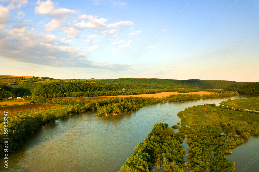 Aerial view of bright river flowing through green meadows in spring.