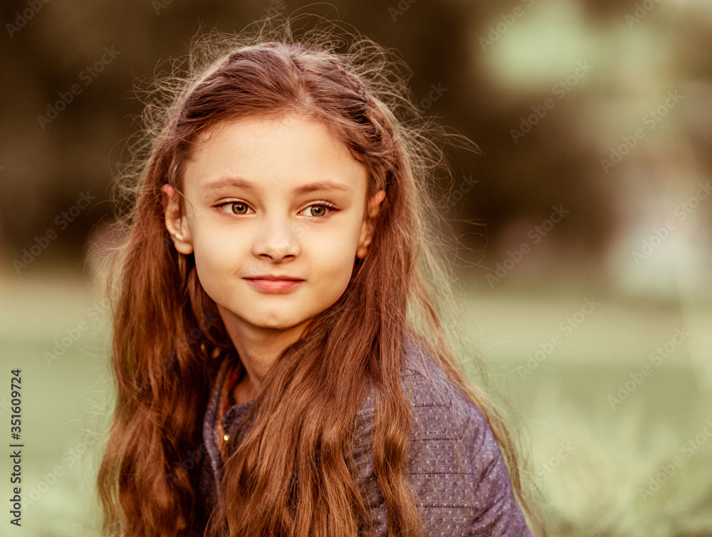 Happy smiling kid girl thinking with long curly hair on summer sunset grass background. Closeup Happy smiling kid girl thinking with long curly hair on summer sunset grass background. Closeup