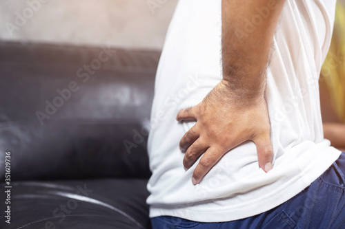 Young Man Sitting in living room suffering from back pain on sofa suffering from painful periods concept. 