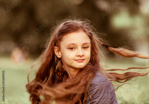 Happy smiling kid girl waving long hair on summer grass background. Closeup