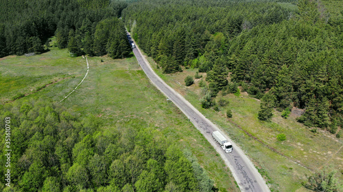 Aerial. Commercial truck leaves the forest terrain. View above from drone.
