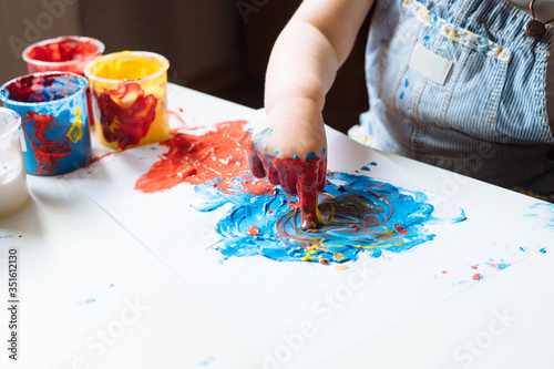Child painting with her hands on the table at home using blue and red paint. Finger painting or art therapy for children. Fun activities for toddlers. Close up.   photo