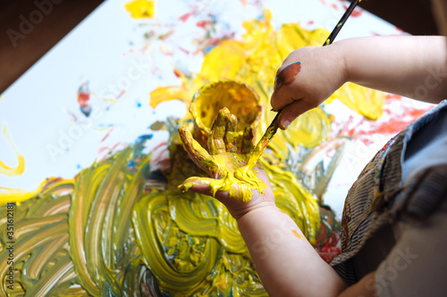 Child painting her hand with yellow paint and paintbrush. Finger painting or art therapy for children. Fun activities for toddlers.  