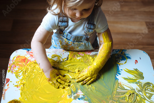 Child painting with her hands on the table at home using yellow paint. Finger painting or art therapy for children. Fun activities for toddlers.  