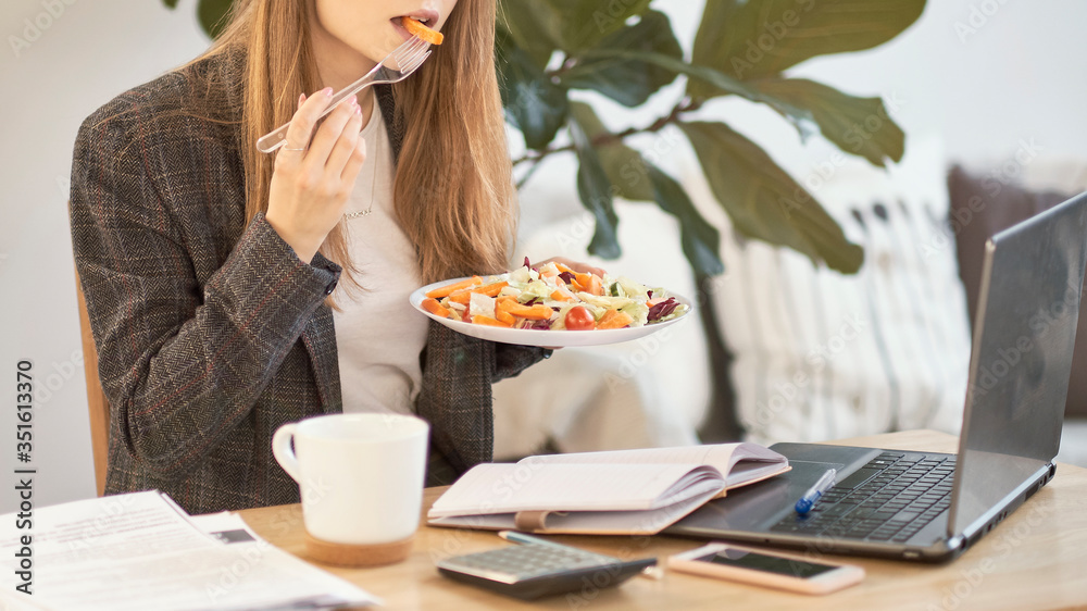 Unrecognizable young business woman having a lunch break at desk, she is eating fresh salad, person