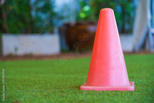 One red plastic small traffic, sport cone for on artificial green grass in the small indoor stadium and blur background.