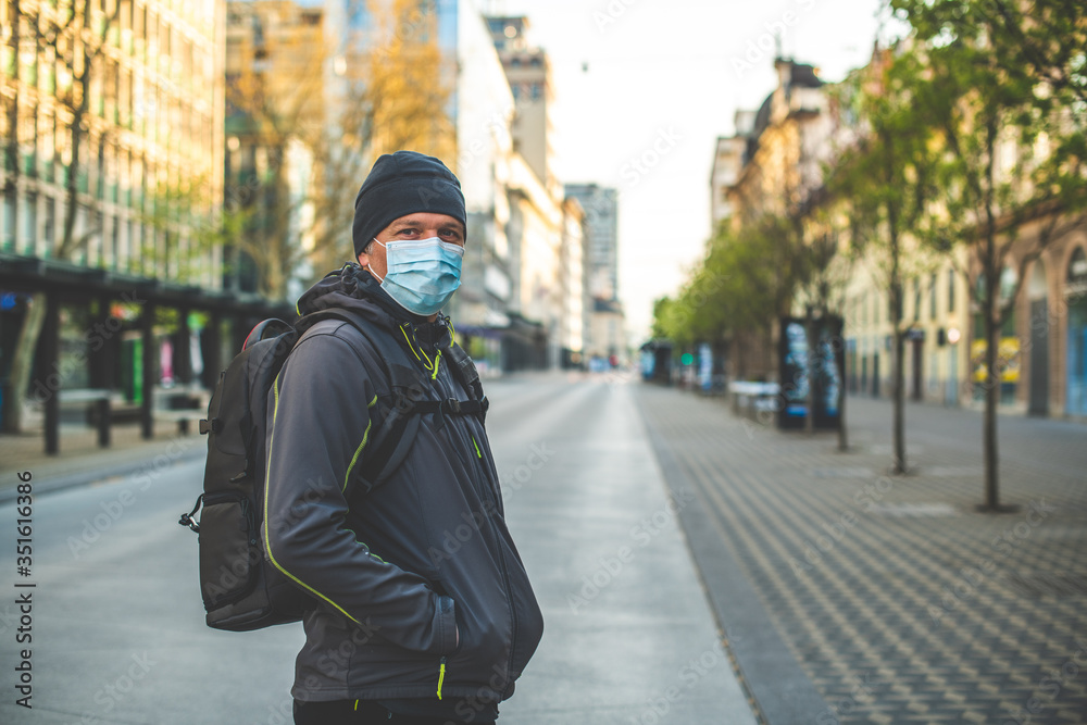 Fototapeta premium Close up of a Caucasian man, with cap and backpack, and with mask on his face, standing on a deserted street
