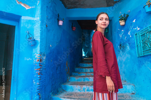 Morocco girl in national dress stands at the entrance to the tunnel with steps in the blue city. © nelen.ru