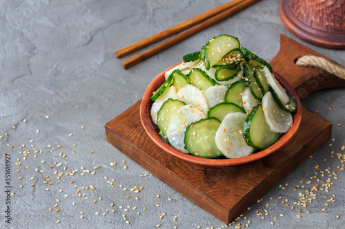 Japanese sunomono pickled cucumber and daikon salad sprinkled with sesame seeds   on  gray concrete background  with copy space photo