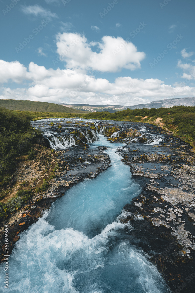 Fototapeta premium Incredible view of Bruarfoss Waterfall. The 'Iceland s Bluest Waterfall.' Blue water flows over stones. Midnight sun of Iceland. Visit Iceland. Beauty world.